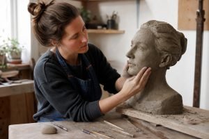 Vajarka oblikuje skulpturu od gline